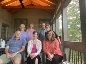 FUUSN's Ministerial Search Committee, a group of seven adults, three seated and four standing behind them on a porch with trees in the background.
