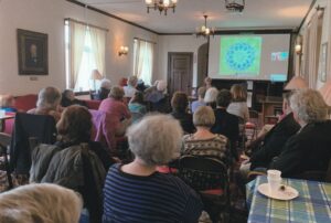 Over 60s club gives a presentation in the Alliance Room. A large number of adults seated on folding chairs with a presentation being projected onto a screen.