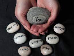 Two cupped hands hold a gray stone with the word "You" printed on it. Several other stones surround the hands, with the words, "Meaning, Connection, Love, Comfort, Hope, Peace, and Strength" written on them.