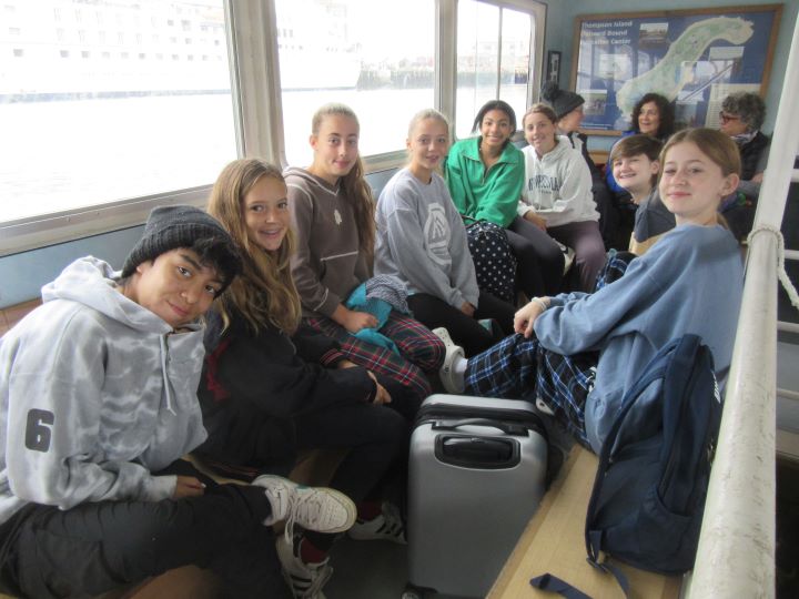 A group of young teenagers in sweatshirts and hoodies and three adults ride a ferry to Thompson Isle.