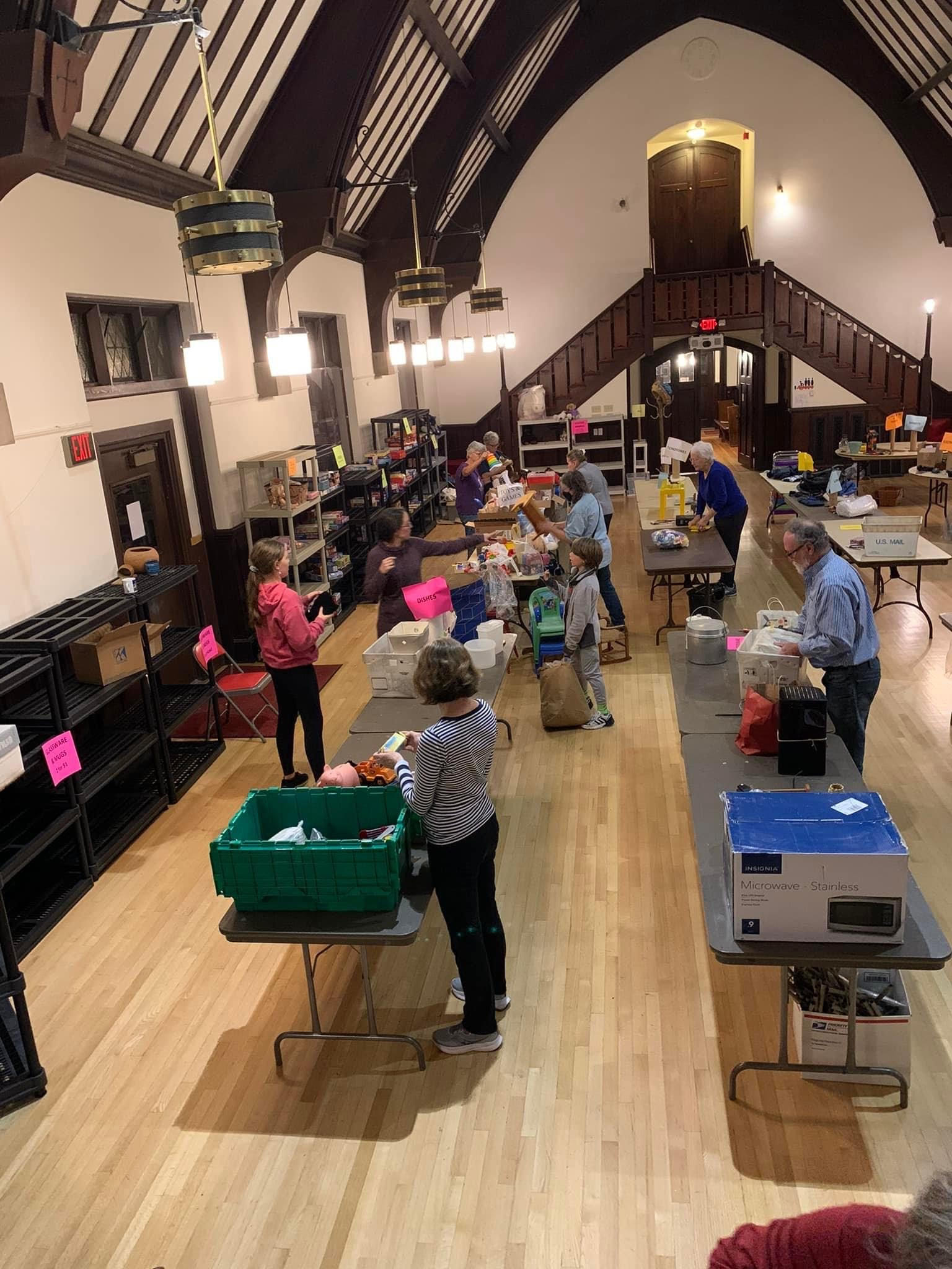 Volunteers begin setting out items on long folding tables and empty shelves in the Parish Hall.