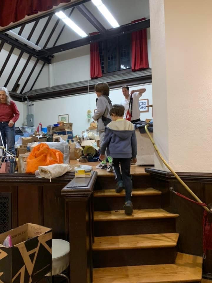Two children climb the steps up to a stage where two adult volunteers are sorting items for the yard sale.