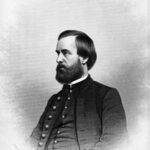 Black and white portrait of a man in his late 30s with dark hair and beard wearing Civil-War-era jacket, waistcoat, and shirt.