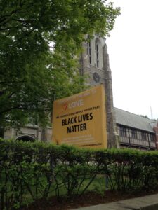 A bright yellow banner stating, "Black Lives Matter" stands in front of a church.