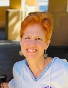 a white woman with short red hair and a light blue top smiles at the camera