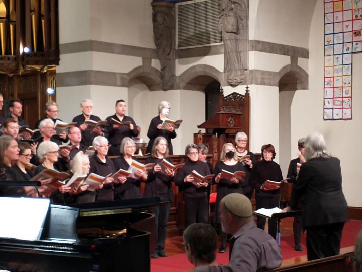 A large choir stands at the front of the sanctuary, directed by a gray-haired woman dressed in black.