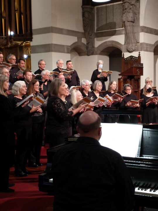 A large choir sings at the front of the Sanctuary, accompanied by a male pianist at a grand piano.